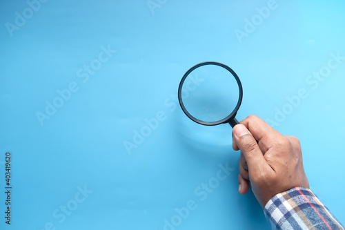  hand holding magnifying glass on blue background 