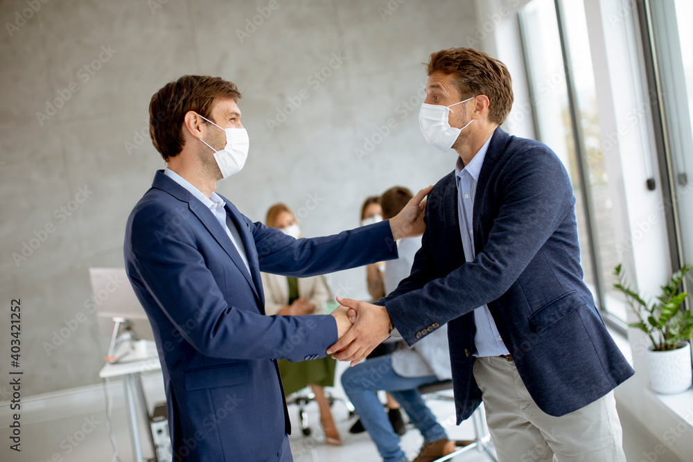 Young business men handshaking in the office with protective facial masks