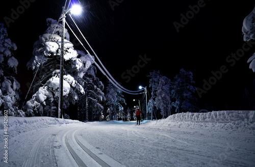 Person skiing in a cross country slope through an idyllic lit forest at night. photo