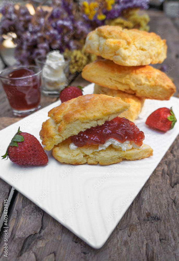 Scones and Strawberry Jam, Clotted cream in a white plate on a wooden table Scones and Strawberry Jam, Clotted cream in a white plate on a wooden table