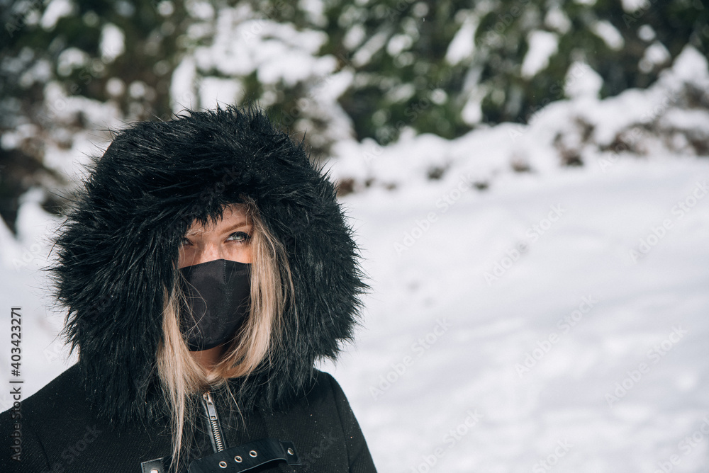 retrato de mujer rubia con abrigo negro, mascarilla negra y ojos azules en la nieve en un día soleado retrato de mujer rubia con abrigo negro, mascarilla negra y ojos azules en la nieve en un día soleado