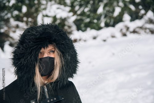 retrato de mujer rubia con abrigo negro, mascarilla negra y ojos azules en la nieve en un día soleado © Safi