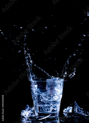 Water splashes. Fall of ice cubes in a glass with clear water on a black background