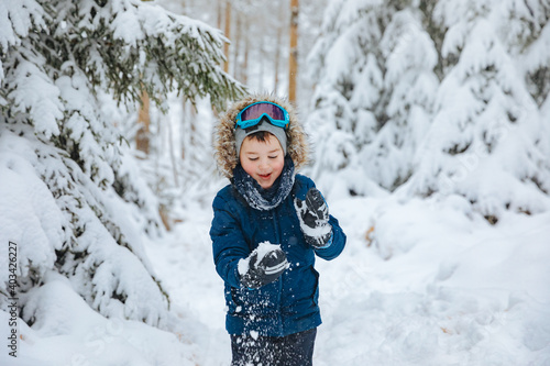 boy in a ski suit and ski goggles stands on a ski slope. Child in winter in the forest 
