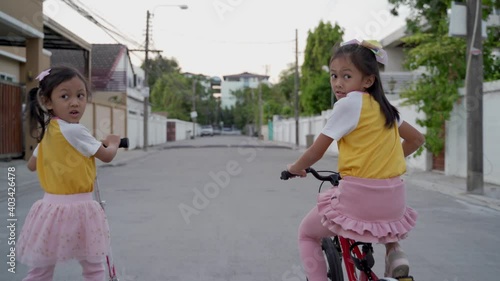 asian sister wearing same dress playing around the neighborhood. children riding bicycle and scooter on street around home area. kid having activity in the evening. 