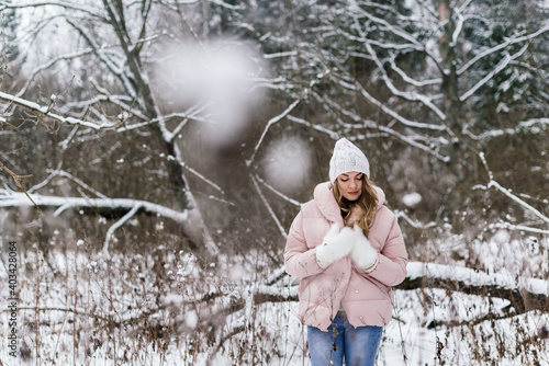 young beautiful woman in warm clothes in a snowy park, among the bare snow-covered branches and tall dry grass in winter