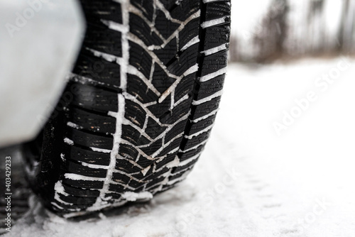 New winter tire in a silver car standing on a snow-covered road in the forest, a visible tread with snow.