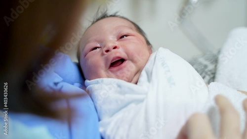 asian female parent holding newborn baby with care on bed at hospital. woman looking at infant.