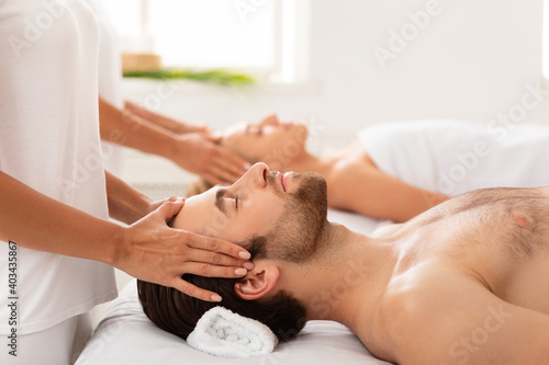 Spouses Receiving Head Massage Lying With Eyes Closed At Spa