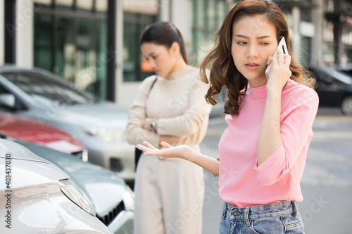 Two women at car accident site, one is using mobile phone to call someone