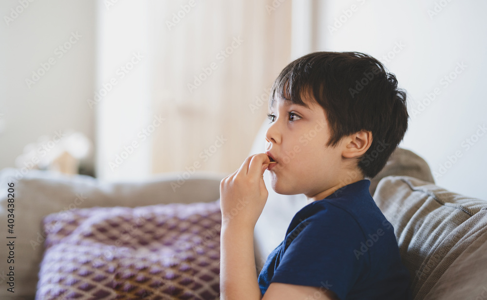 Portrait New normal lifestyle Kid siting on sofa eating potato crisps while watching TV, Young boy eating snack while watching cartoon, Child stay at home during social distance from Covid-19 Portrait New normal lifestyle Kid siting on sofa eating potato crisps while watching TV, Young boy eating snack while watching cartoon, Child stay at home during social distance from Covid-19
