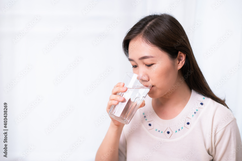 Cheerful Asian young woman drinking a water in a glass close up with copyspace. Asian working woman holding a glass of drinking water and smiling to camera. Work life balance concept. Healthy woman Cheerful Asian young woman drinking a water in a glass close up with copyspace. Asian working woman holding a glass of drinking water and smiling to camera. Work life balance concept. Healthy woman