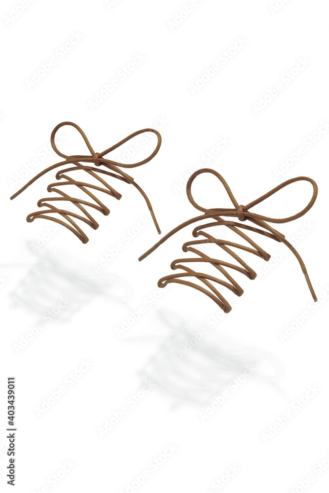 Fototapeta premium Subject shot of beige shoe strings with thin tips. The plaited shoe laces are tied in a bow and hanging in the air on the white background. 