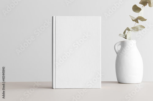 White book mockup with a eucalyptus in a vase on a beige table.