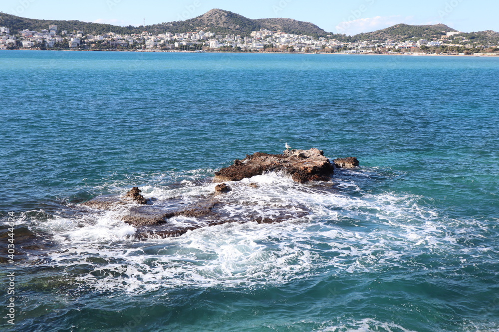 Fototapeta premium Waves splashing on the rocks in the sea while a seagull is sitting on the rocks relaxed. 