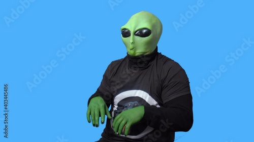 Professional artist in alien costume and in a black t-shirt laughs and clutches his head in hysteria against blue chromakey background. Role rehearsal. photo