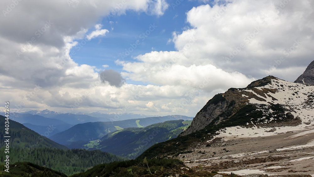 A panoramic view on the Alpine peaks in Austria from the Marstein. The slopes are still partially covered with snow. Stony and sharp mountains. Overcast. Baren slopes, green valley below. Serenity