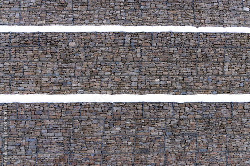 Metal Cage filled with rocks and snow texture . Stone wall with metal grid as background.  Gabion net