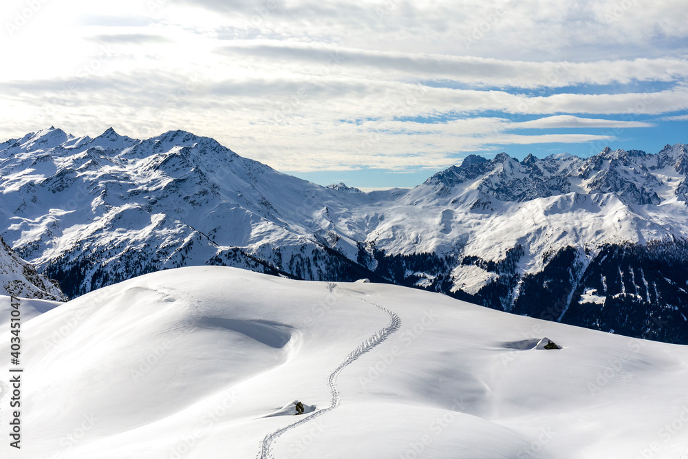 Single ski mountaineering tracks on a white snow-covered plateau in winter above Verbier in Switzerland. Single ski mountaineering tracks on a white snow-covered plateau in winter above Verbier in Switzerland.