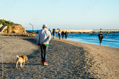 Uomo che passeggia con il cane sulla spiaggia in un pomeriggio di autunno photo