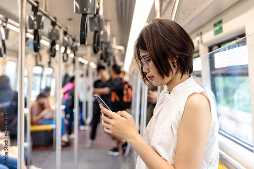 Asian young short hair woman wearing glasses using and looking her smartphone in train