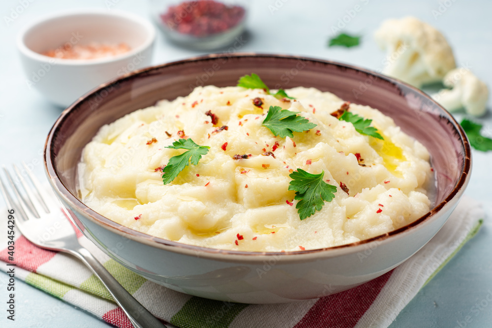 Mashed cauliflower with butter, pink peppercorns and parsley on concrete background Mashed cauliflower with butter, pink peppercorns and parsley on concrete background