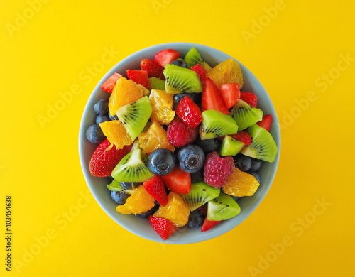 Fruit salad in a bowl on yellow background  kiwi  orange  strawberry  blueberry 