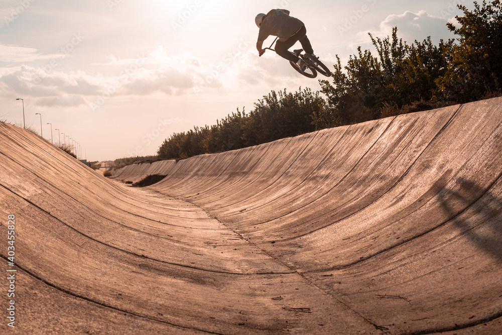 young bmx rider wearing a white helmet jumping on a ramp with the bike