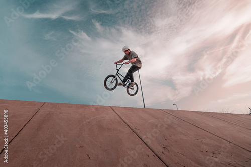 young bmx rider wearing a white helmet jumping on a ramp with the bike