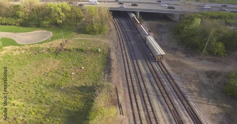 Drone Aerial View and Shot Looking Down on Train Moving Under Car Interstate Highway Overpass on Industrial Steel Railroad Tracks Near Urban Cityscape Landscape Setting Drone Aerial View and Shot Looking Down on Train Moving Under Car Interstate Highway Overpass on Industrial Steel Railroad Tracks Near Urban Cityscape Landscape Setting