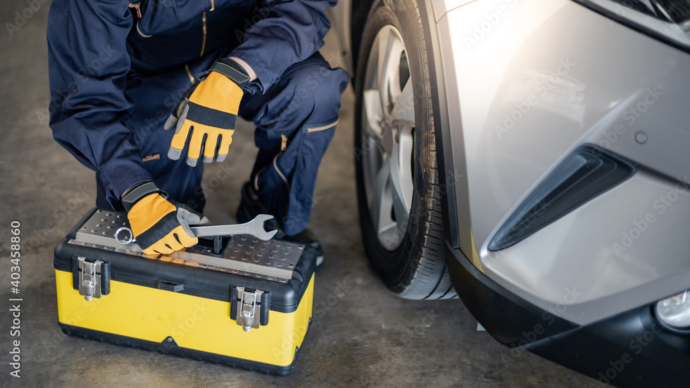 Fototapeta premium Auto mechanic with tool box and wrench checking car wheel and tire in auto service garage. Mechanical maintenance engineer working in automotive industry. Automobile servicing and repair concept