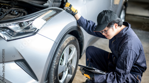 Asian auto mechanic holding digital tablet checking car wheel and tire in auto service garage. Mechanical maintenance engineer working in automotive industry. Automobile servicing and repair concept