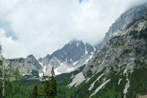 A panoramic view on the Alpine peaks in Austria from the Marstein. The slopes are still partially covered with snow. Stony and sharp mountains. Overcast. Baren slopes, dense forest at the foothill. photo