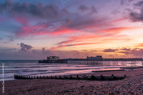 Ribbons of red-lit clouds stretch across the sky above the shore and sea at Worthing, Sussex, UK
