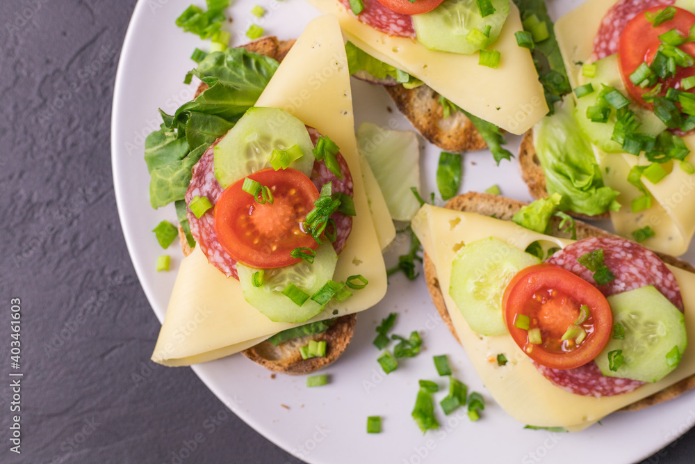 Spring healthy sandwiches with cheese, lettuce and tomato sprinkled with chives on plates lying on a dark background Spring healthy sandwiches with cheese, lettuce and tomato sprinkled with chives on plates lying on a dark background