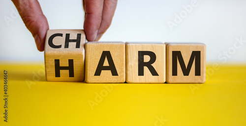 From harm to charm. Male hand turns the cube and changes word 'harm' to 'charm'. Beautiful yellow table, white background. Business and harm or charm concept. Copy space.