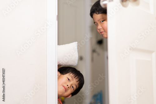 Playful brothers are peeking from behind the door.