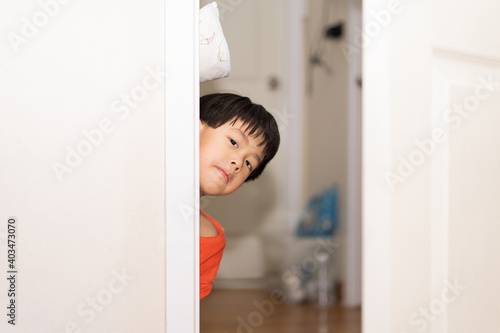 A playful boy peeking from behind the door.