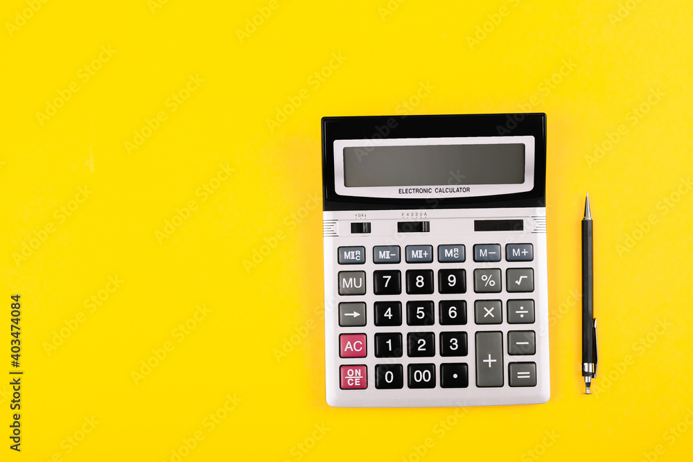 Big silver calculator with gray and black buttons and black pen on a yellow background. Conceptual photo of calculations, accounting, computing, profit, loss, tax. Big silver calculator with gray and black buttons and black pen on a yellow background. Conceptual photo of calculations, accounting, computing, profit, loss, tax.