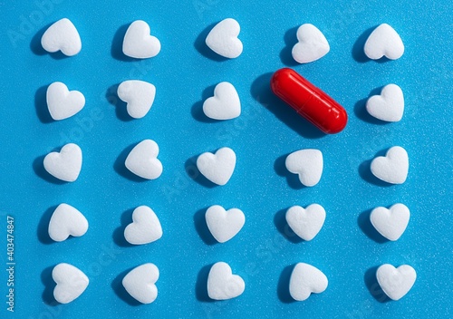 heart-shaped tablets and red pill. pattern on blue background. medicine, cardiology, health. top view, flat lay