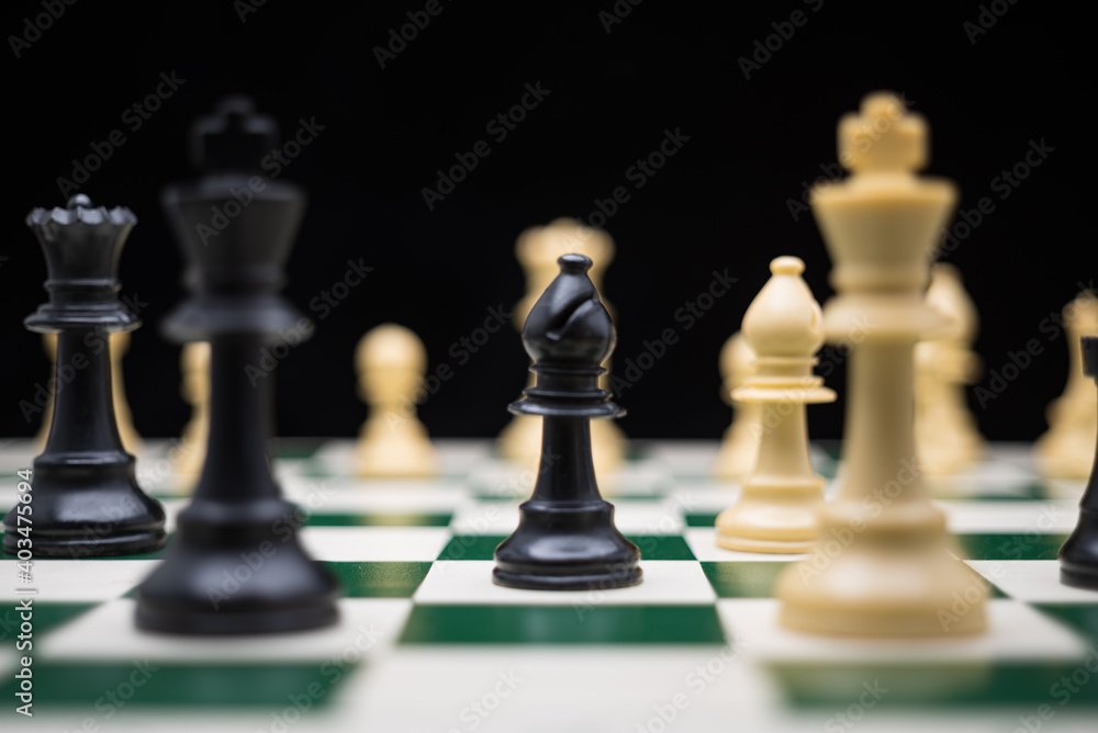 Extreme close up of chess pieces arranged on a portable chessboard before a black background.