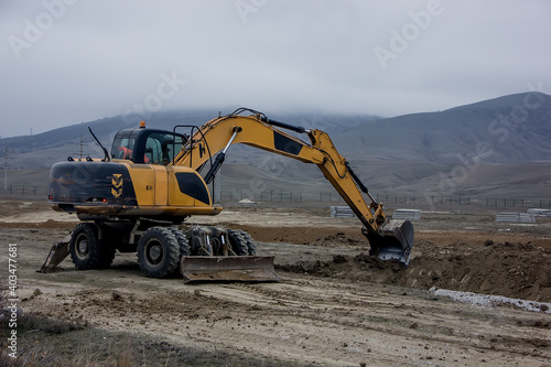 Yellow excavator digs a trench against the backdrop of mountains.