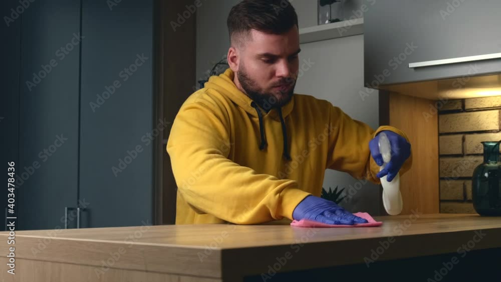 Caucasian man with beard is disinfecting the table using alcoholic spray and gloves Caucasian man with beard is disinfecting the table using alcoholic spray and gloves