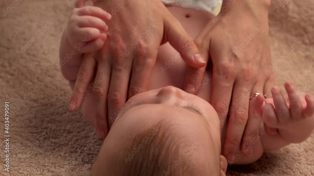 Caucasian mother is massaging the entire body of her newborn girl lying on the blanket Caucasian mother is massaging the entire body of her newborn girl lying on the blanket