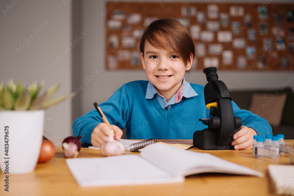 Distance online education, internet learning. First grade boy studying at home using microscope, making notes, biology online lesson Distance online education, internet learning. First grade boy studying at home using microscope, making notes, biology online lesson