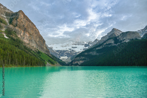 The iconic and stunning Lake Louise in Canada, Alberta, Banff Jasper National Park on a cloudy summer day with stunning emerald, turquoise green water below cascading mountains. 