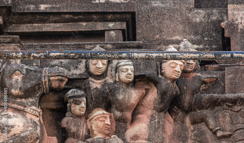 Hampi, Karnataka, India - November 5, 2013: Sri Krishna temple in ruins. Closeup of group of sculpted beige male faces and horse against molded wall under iron bar.  photo