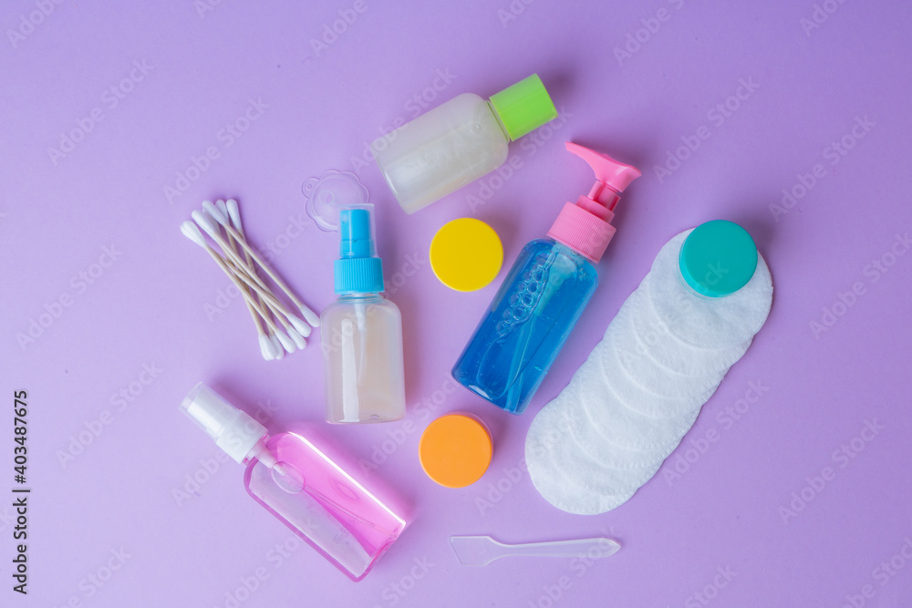 Set of plastic travel bottles on lavender background. Travel kit with approved airplane hand luggage bottle size. Travel containers with colorful tops, sanitizer, cotton pads and cotton swabs. Set of plastic travel bottles on lavender background. Travel kit with approved airplane hand luggage bottle size. Travel containers with colorful tops, sanitizer, cotton pads and cotton swabs.