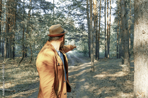 a man in a hat stands with his back to us and shows the way out of the forest