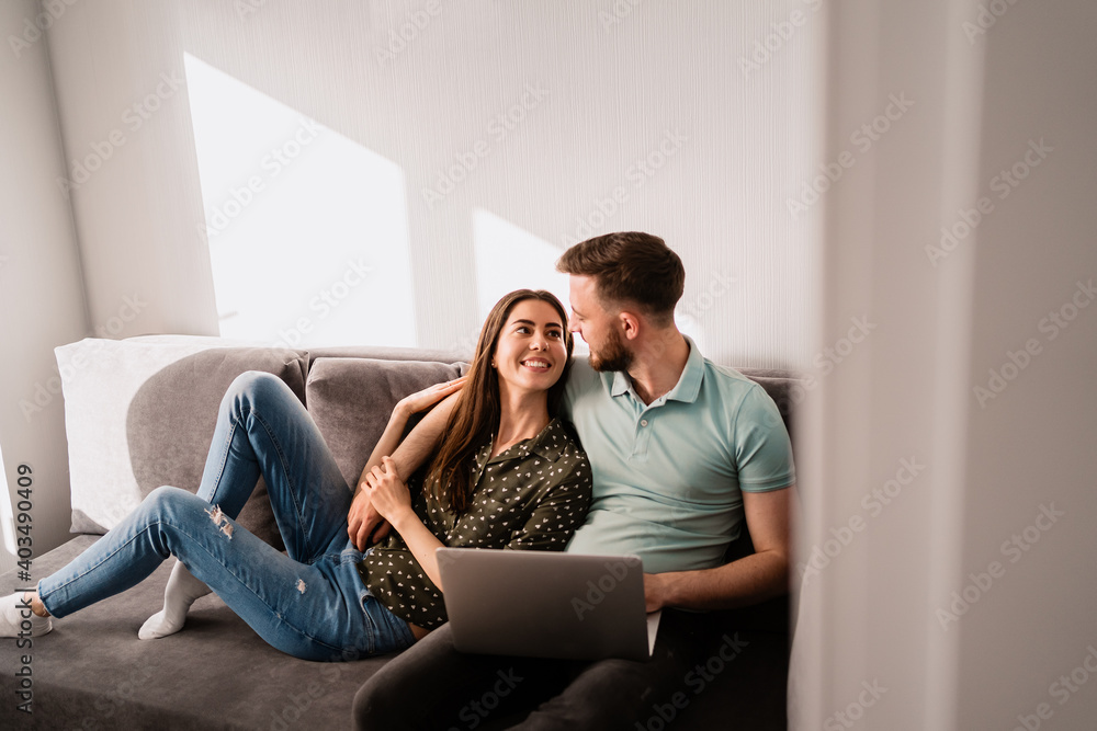 Smiling couple relaxing on the sofa with a notebook hugging each other